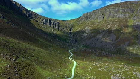 Luftaufnahme-Eines-Schroffen-Bergtals-Und-Eines-Gewundenen-Pfads,-Der-Im-Sommer-Zu-Einem-Felsigen-Wasserfall-Im-Süden-Irlands-Führt