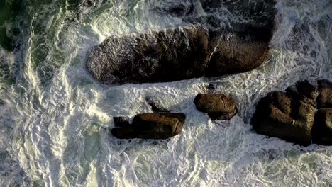 Beautiful-Cinematic-Cenital-Gentle-Rise-Shot-of-Rough-Ocean-Waves-Hitting-Rocks-During-Sunset-at-Cape-Town's-Camps-Bay-Beach