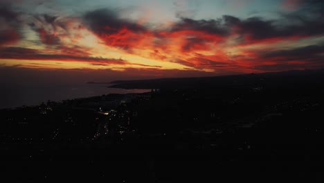 Aerial-Of-Dramatic-Orange-Red-Sunset-Through-The-Cloud-With-Silhouette-Of-Coastline-Below