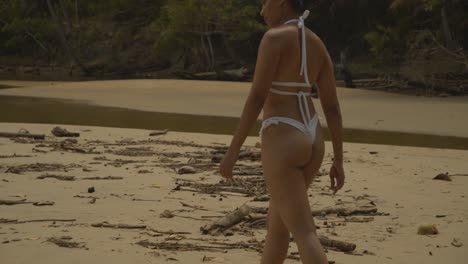 A-woman-in-a-micro-bikini-walking-towards-the-mouth-of-the-river-before-turning-around-at-the-end