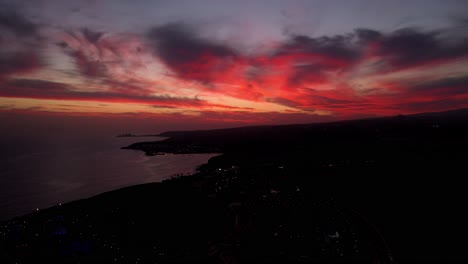 Drone-of-Las-Palmas-Gran-Canaria-at-nightfall-with-fiery-vibrant-red-clouds,-aerial-at-sea