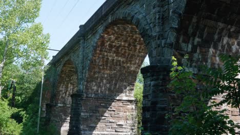 Water-reflections-of-sunlight-under-stone-train-bridge,-Wissahickon-Creek
