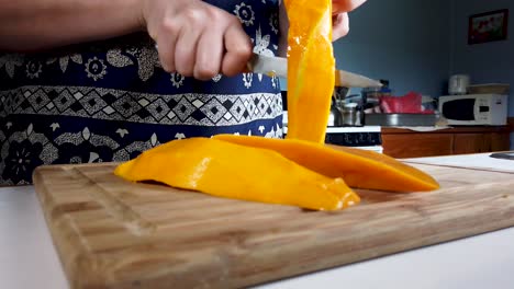 Woman-uses-knife-to-slice-a-large-fresh-mango,-removing-the-pit