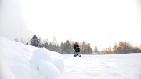 Static-slow-motion-shot-of-father-walking-with-baby-stroller-in-snowy-winter-storm