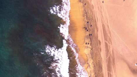 Top-down-drone-view-of-waves-breaking,-people-swimming-at-sunny-beach,-Gran-canaria,-las-palmas