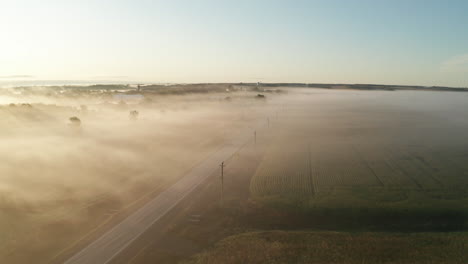 Cars-drive-on-a-rural-highway-with-a-blanket-of-low-morning-fog-on-the-landscape