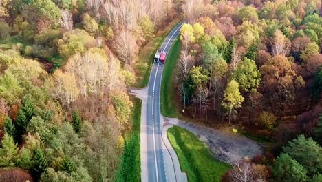 Luftaufnahme-Von-Zwei-Lastwagen,-Die-Auf-Einer-Straße-In-Einem-Farbenfrohen-Herbstwald-Fahren