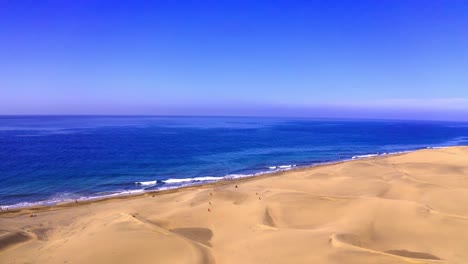 High-dunes-and-blue-beach-drone-flight-in-clear-blue-sky-aerial-flying-over-las-dunas-at-las-palmas-beach-in-canaries-islands