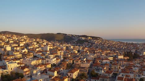 Aerial-sunrise-drone-Flight-over-downtown-mitilini-circling-reveal-to-houses-on-hills,-mountains-at-sea-with,-lesvos,-greece
