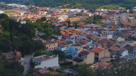 A-panning-view-over-the-beautiful-and-colorful-old-houses-with-green-forest-of-town-of-Capdepera,-Mallorca