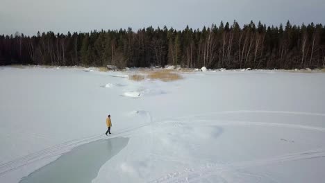 Drone-shot,-following-senior-man-walking-on-frozen-winter-lake-in-Northern-Finland,-far-away-from-civilization