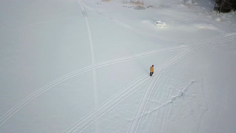Aerial-top-down-view-of-senior-man-walking-in-snow-mobile-trail,-in-snowy-winter-landscape,-tracking-shot-tilting-down,-in-Rovaniemi,-Finland