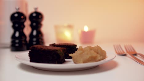 Tasty-looking-romantic-Desert:-Brownies-with-applesauce-on-white-Plate-with-Candles-in-the-Backgound