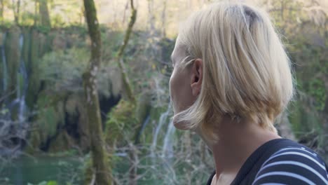 Schönes-Mädchen-Mit-Kurzen-Blonden-Haaren,-Das-Die-Natürliche-Schönheit-Des-Waldes-Und-Des-Wasserfalls-Genießt