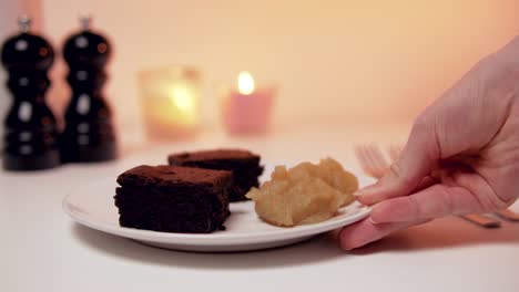 Tasty-looking-romantic-Desert:-Brownies-with-applesauce-on-white-Plate-with-Candles-in-the-Backgound