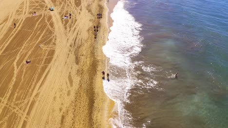 Gran-canaria-beach-flight-over-shoreline-with-tourists-walking-in-clear-blue-sky-aerial-drone-flying-over-dunes-at-las-palmas-beach-in-canaries-islands