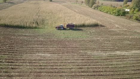 Aerial-reveal-shot-of-tractor-harvesting-crops-on-wide-green-field