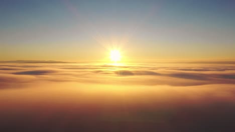 Drone-aerial-flight-to-sun-at-sunrise-above-clouds,-panning-heavenly-sky-panorama