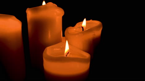 Group-of-four-candles,-orange-fire-composition-on-black-background-slow-motion