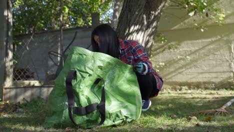 asian-girl-putting-dry-leaves-to-bag,-still-low-angle-shot