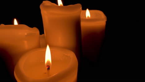 Group-of-lit-candles-with-orange-flame,-four-candles-on-black-background-in-slow-motion