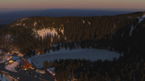 Flyover-shot-over-the-frozen-black-forest-lake-called-Mummelsee-at-Sunset-in-Winter