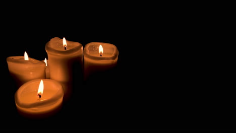 Group-of-four-lit-candles-on-black-background,-orange-fire-and-candles