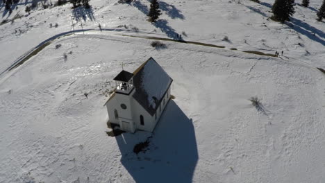 Aerial-of-Church-on-a-Snowy-Mountain-field,-pull-back-to-reveal-landscape