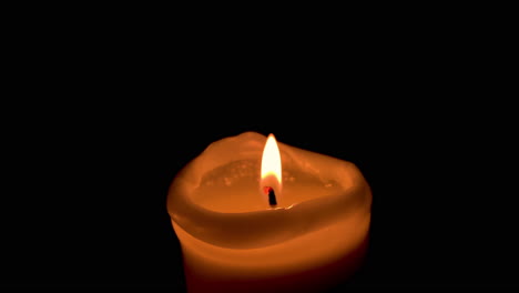 Close-up-on-one-lit-candle,-orange-flame-on-black-background
