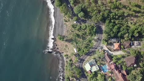 Luftaufnahme-Der-Straße-In-Der-Nähe-Des-Felsigen-Strandes-Mit-Ozeanwasser,-Das-Die-Felsen-In-Bali-Spritzt