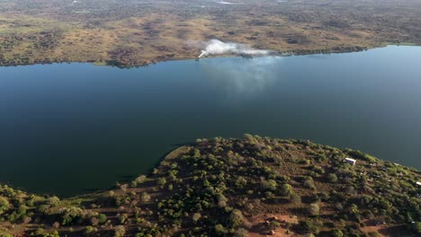 Cinematic-Aerial-Descending-Shot-of-Inhampavala-Lake-in-Chindeguele-Mozambique-During-Golden-Hour-Sunrise-with-Fire-on-Background
