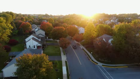 Pick-up-truck-turns-onto-street-through-residential-neighborhood-community,-colorful-autumn-fall-leaves-line-the-road,-evening-glow-or-warm-sunset