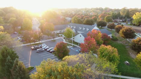 Gorgeous-aerial-drone-shot-in-autumn,-bright-evening-sunset-illuminates-colorful-fall-leaves-on-trees,-community-building,-library-in-Lititz-Pennsylvania