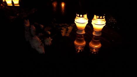 Grab-Brennende-Kerzenreflexion-Mit-Blumen-Auf-Dem-Friedhof,-Dunkle-Nachtatmosphäre-Herauszoomen