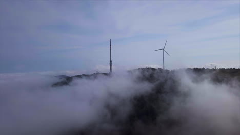 Aerial-shot-of-big-broadcasting-tower-and-wind-generator-wrapped-in-clouds-over-the-black-forest-mountain-Hornisgrinde-on-a-brighty-day-in-Autumn