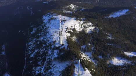 Slow-aerial-tracking-shot-of-a-wind-turbine-and-a-broadcast-tower-on-a-snow-covered-plateau