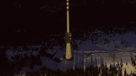 Aerial-tracking-shot-of-big-broadcast-tower-at-sunset-on-the-snowy-mountain-Hornisgrinde-in-the-black-forest