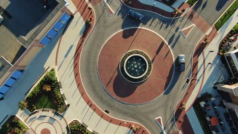 Aerial-top-down-drone-shot-of-traffic-circle-with-cars-entering-and-exiting,-decorative-brick-and-water-fountain