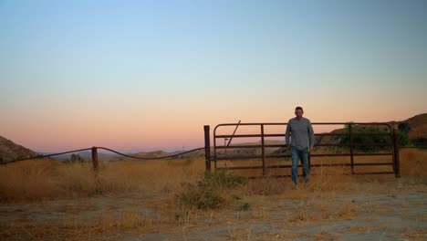 Static-shot-of-a-man-walking-from-a-country-gate,-on-the-Californian-countryside,-at-dusk,-sunny-evening