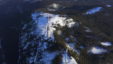 Aerial-tracking-shot-of-a-wind-turbine-and-a-broadcast-tower-on-a-snow-covered-plateau