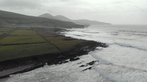 Aerial-of-atlantic-seascape-next-to-sandy-beach,-waves-and-black-rocks