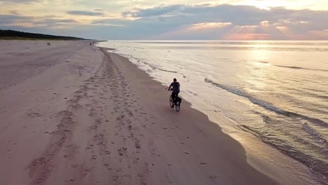 Slowmotion-Shot-of-a-Young-Man-Riding-a-Bicykle-on-Beach-at-Sunset