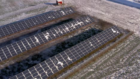 Vista-Aérea-De-Drones-De-Una-Estación-De-Paneles-Solares-Ligeramente-Cubierta-De-Nieve-Que-Alimenta-Una-Granja