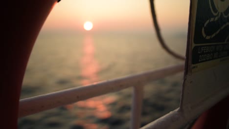 Rack-focus-shot-on-a-vessel-cruising-the-sea-on-sunset-with-the-sun-on-the-background-and-a-life-buoy-on-the-foreground,-Slow-motion,-Greece
