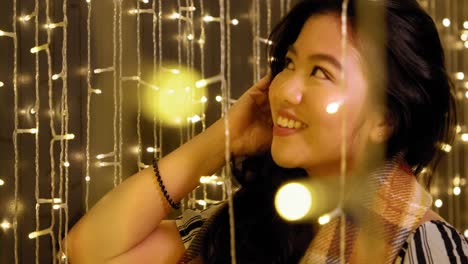 Beautiful-Young-Asian-Filipina-Woman-Smiling-and-Adjusting-Hair-in-warm-yellow-Fairy-Lights-in-4K-slow-motion