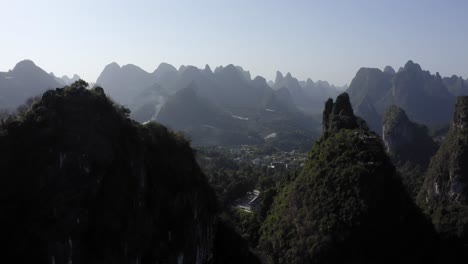 Wide-aerial-shot-of-an-isolated-town-surrounded-by-mountains-in-Yangshuo,-China