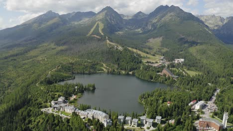 Tilt-Up-Drone-Shot-Alpine-Lake-and-Resorts-on-Mountainside,-High-Tatras-Slovakia