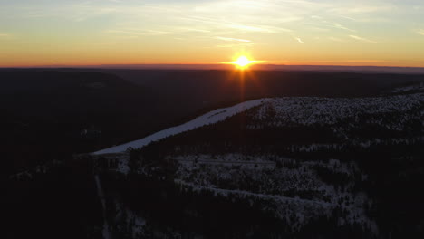 Aerial-panning-shot-over-a-ski-run-at-sunrise-on-a-snowy-black-forest-mountain-top-at-clear-weather