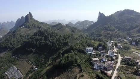 Rising-aerial-shot-of-an-isolated-town-surrounded-by-mountains-in-Yangshuo,-China