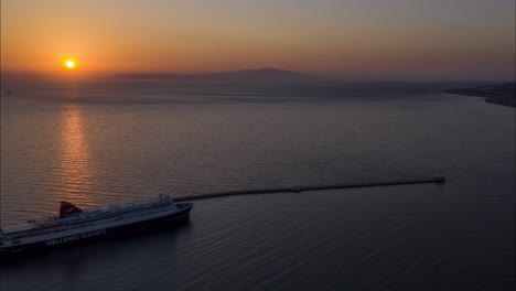 Drone-Sunrise-View-Of-The-mediterranean-sea-Over-Water-With-Mountains-and-ferry-to-athens-in-lesvos,-Greece---mitilini-harbor-Aerial-hyperlapse